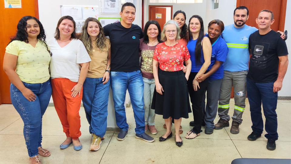 Foto colorida dez colegas de trabalho em pé, abraçados para uma foto.